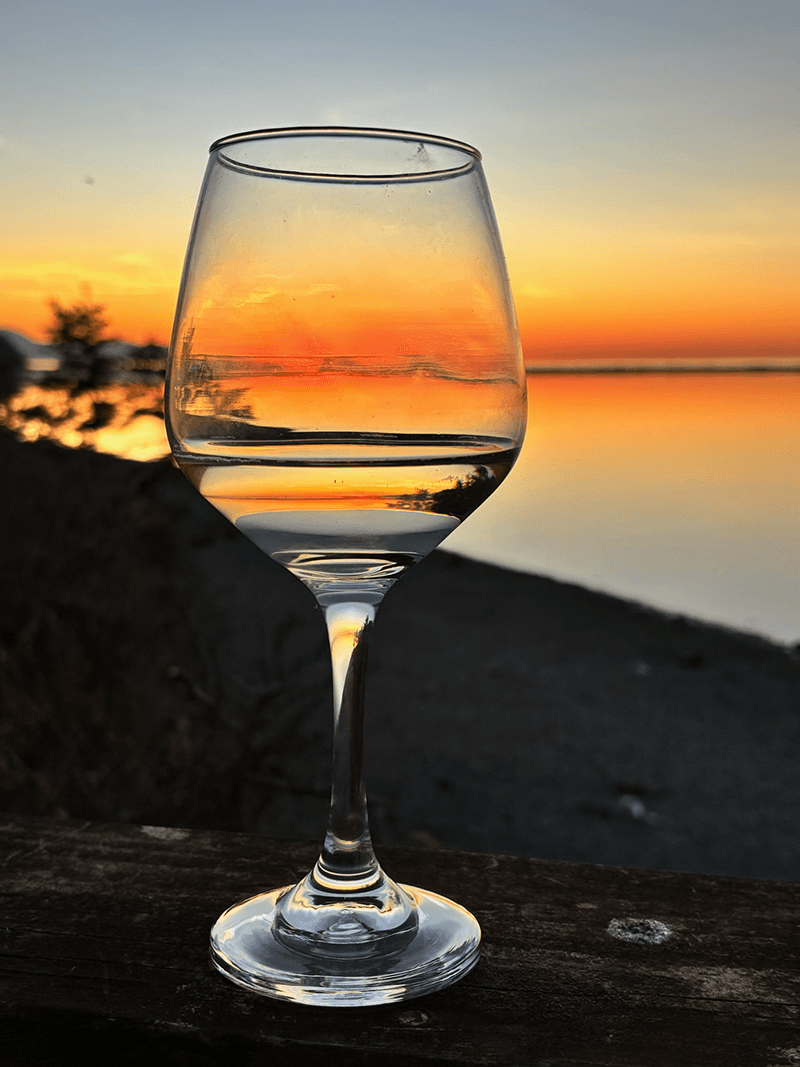 A wine glass reflects a vibrant sunset over a calm body of water.