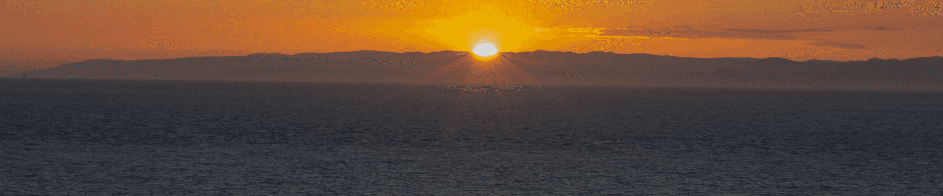 Sunset over the ocean with golden hues and distant mountains.