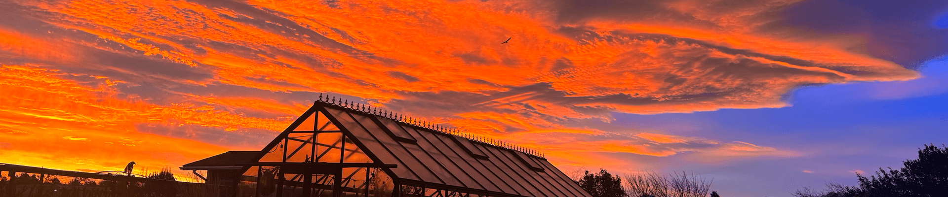 A vibrant sunset casts orange and blue hues over a silhouetted building with a triangular roof.